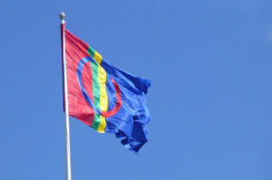 Det samiske flagget vaiende i vinden på himmelblå bakgrunn.