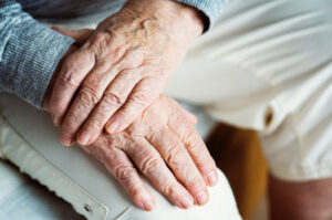Hendene til en eldre person foldet over hverandre på et kne.