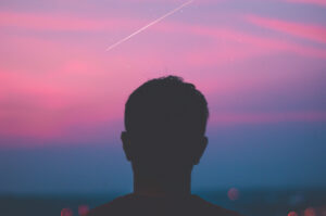 Silhuett av hode til en person mot en vakker rosa og blå kveldshimmel. Kondensstripen til et fly kan skimtes på himmelen.