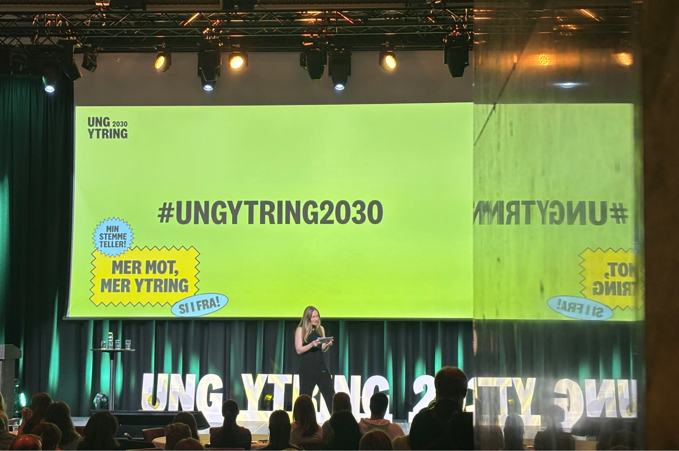 Person på en scene foran en grønn skjerm med teksten #UNGYTRING2030