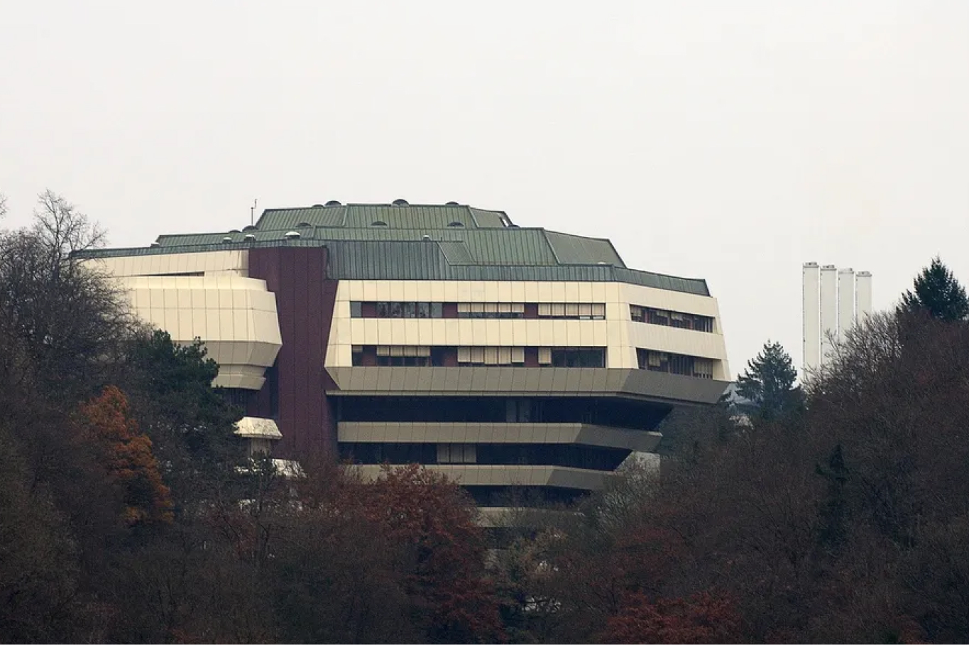 Postmodernistisk bygning som stikker opp bak en skogkledd park.